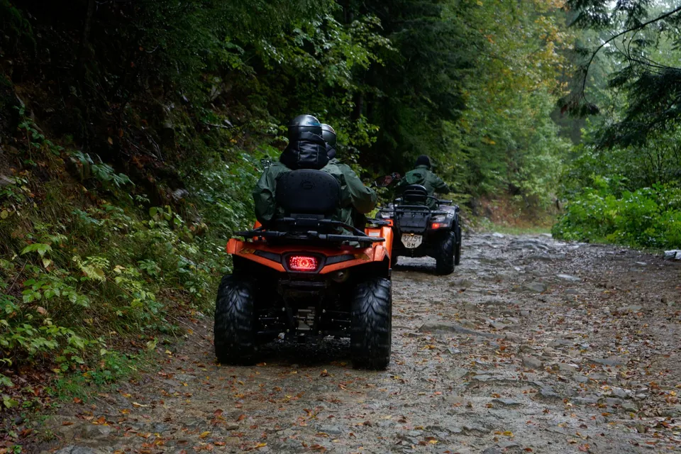 Deux quads progressent sur un chemin de terre en forêt