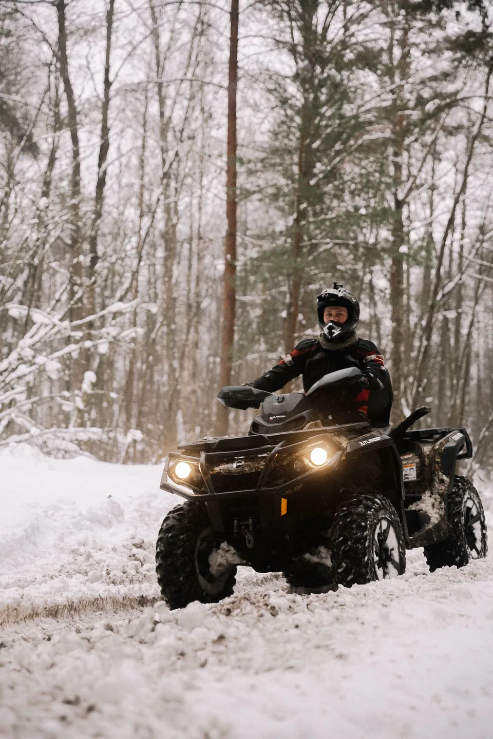 Pilote casqué sur un quad dans une forêt enneigée